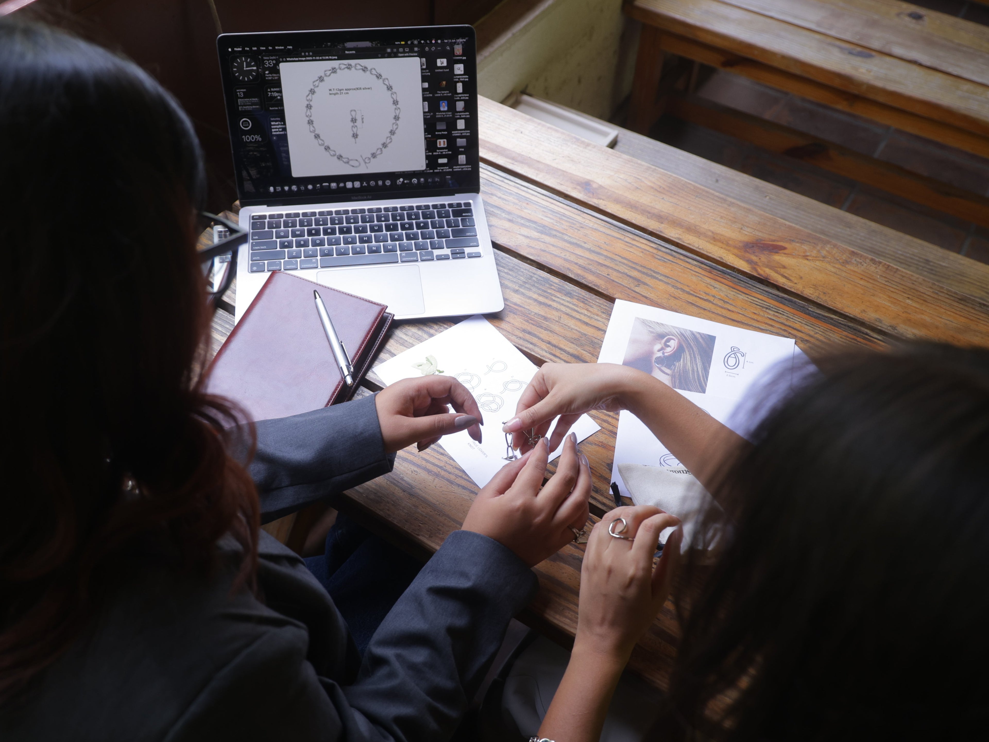 Two people sitting at a wooden table with a laptop and books, engaged in an activity.
